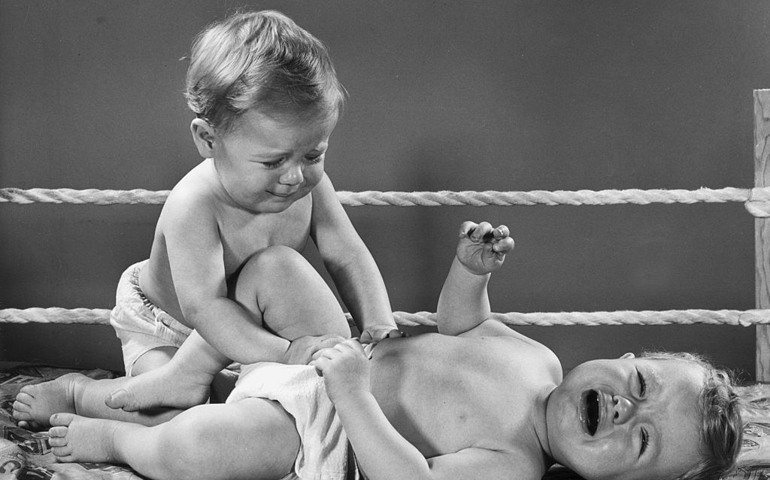circa 1945: An infant lays on his back, crying, as another crying baby pushes on the infant's stomach. Rope is strung behind them to resemble a wrestling ring.