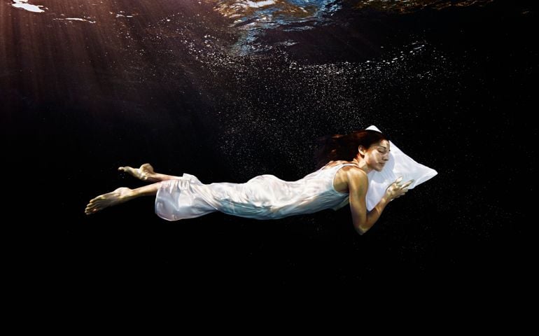 Woman in nightgown with head on pillow sleeping underwater