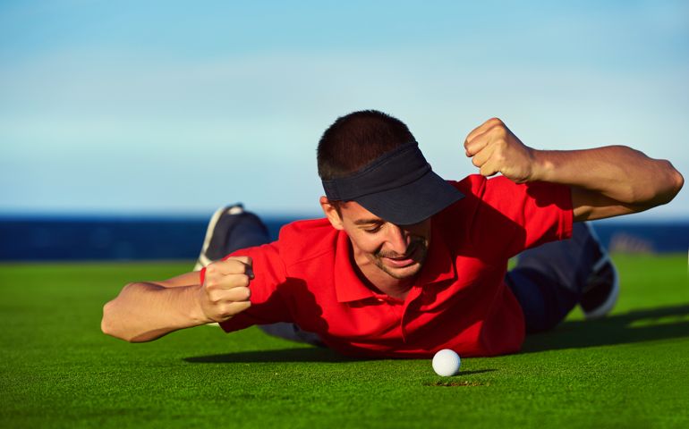 golfer man angry for his lost, golf ball near the hole, he lying down and looking at it with furious expression.