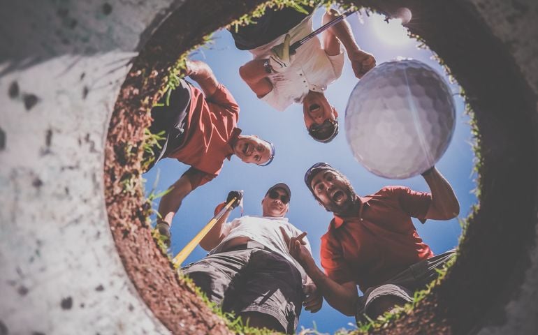 A Point Of View picture of 4 Golf Players and Golf Ball view From Inside the Hole on a sunny day of summer. The players are excited and happy.