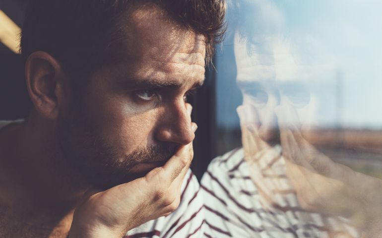 Sad young man looking through the window