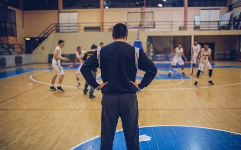 Basketball coach watching his players on training, rear view.
