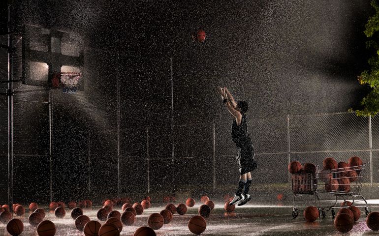 Man shooting basketball at night in rain, side view