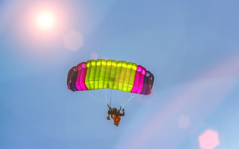 people skydiving with a multicolor parachute at sunset