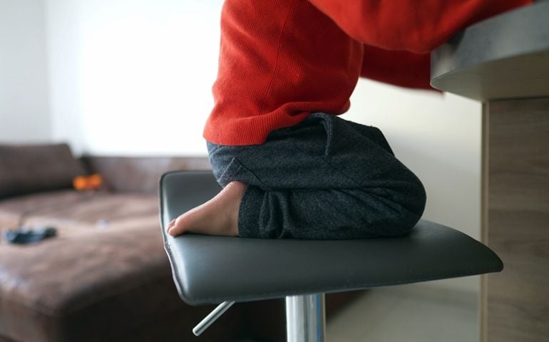Restless child sitting on kitchen stair stool. One hyper active little boy at home in high chair