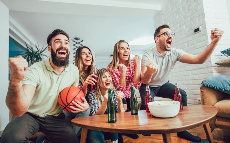 Happy friends or basketball fans watching basketball game on tv and celebrating victory at home.