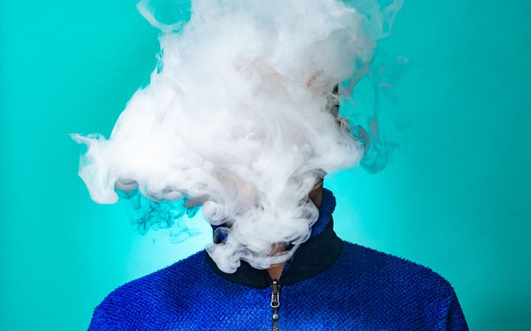 A masked man smoking vape and exhaling