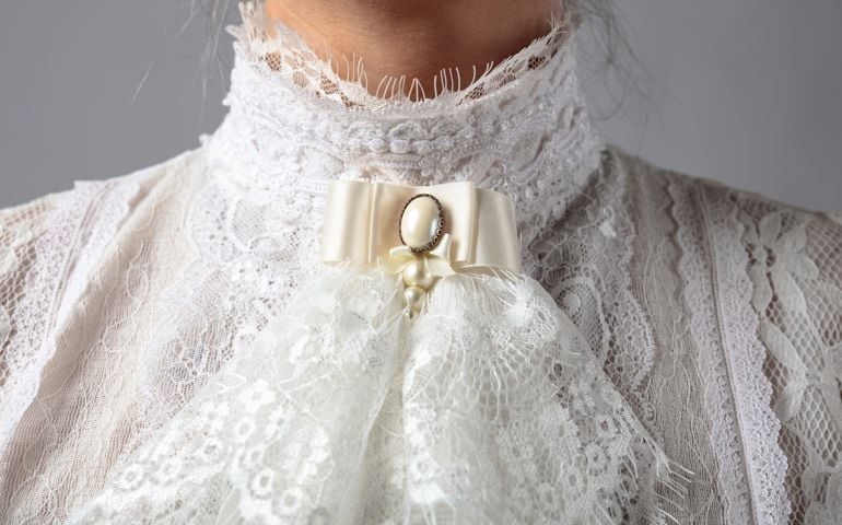 Fragment of a Victorian dress with a brooch. White blouse with lace, embroidery and high collar.