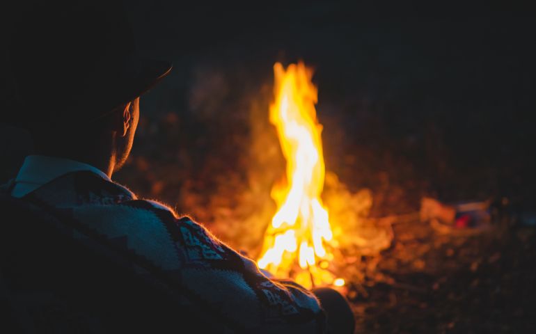 Man in traditional native american poncho and hat sits by the fire in the wood