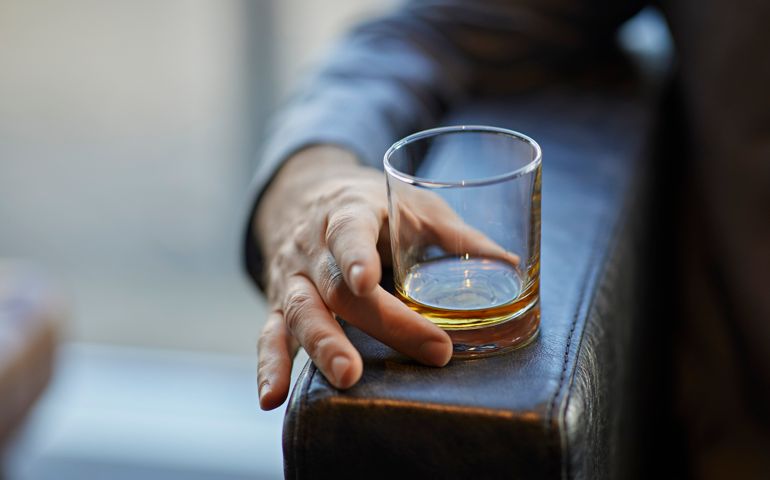 Close-up of man with whiskey glass on arm rest of a leather chair