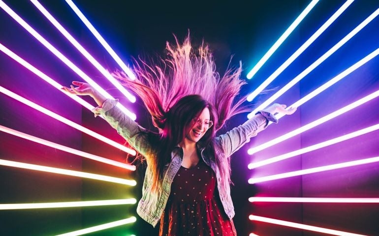 Attractive dancing girl, hair flying, neon light. Portrait of girl posing with hands up.