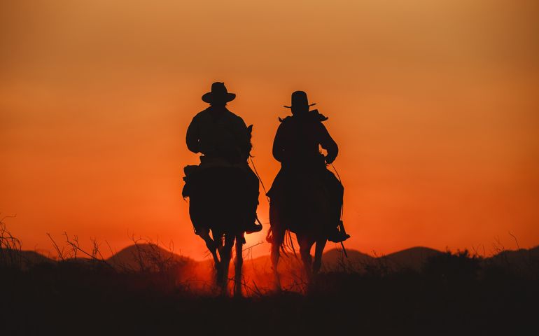 Silhouette the cowboy riding on a mountain with an yellow sky.