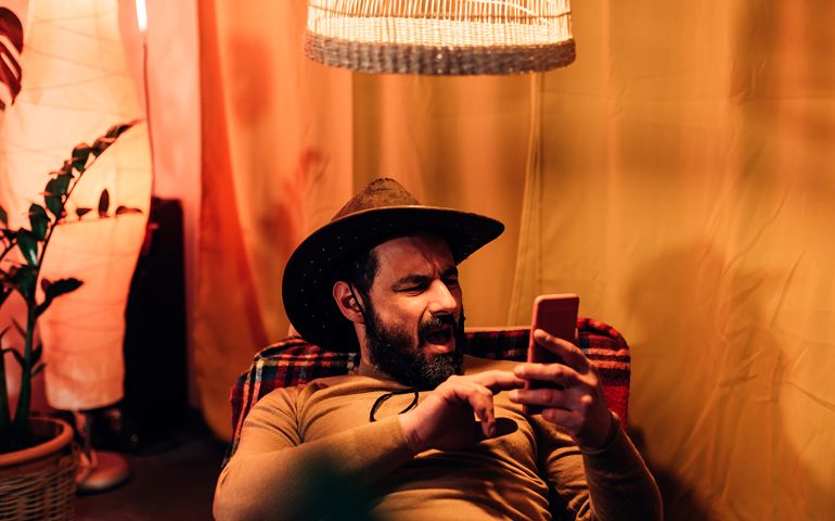 portrait of a shocked man holding a cell phone and reading something on the telephone screen. Male person lying on a chair at home and using mobile