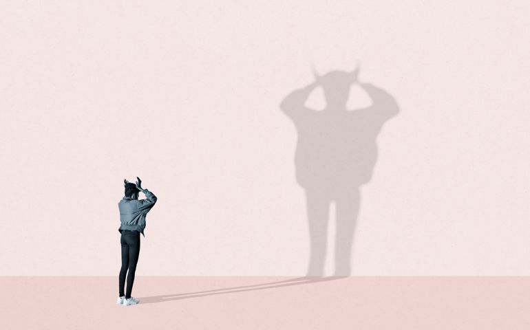 Rear view of young woman making large devil shadow on pink background