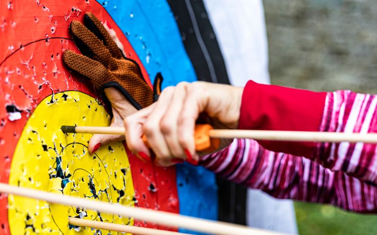 Mature woman shooting bow outdoors on autumn day. Target on an archery field