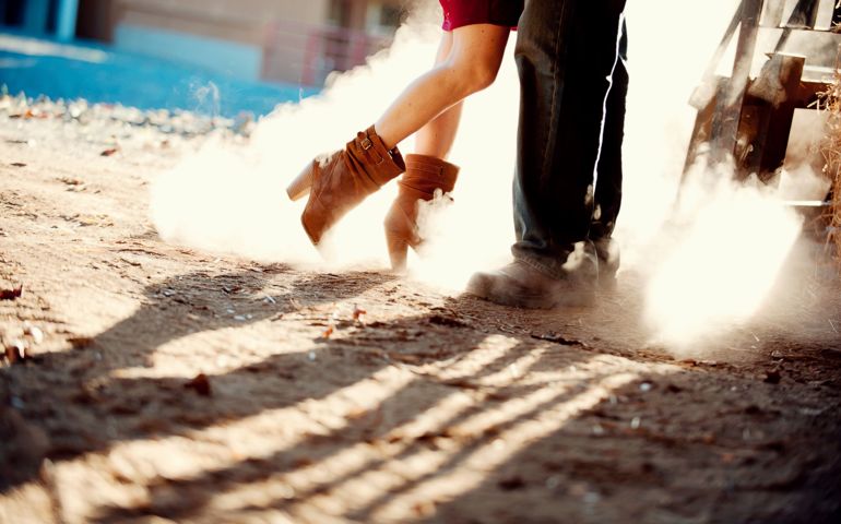 Man and woman close together in a dusty farm environment. Dusty cowboy boots.