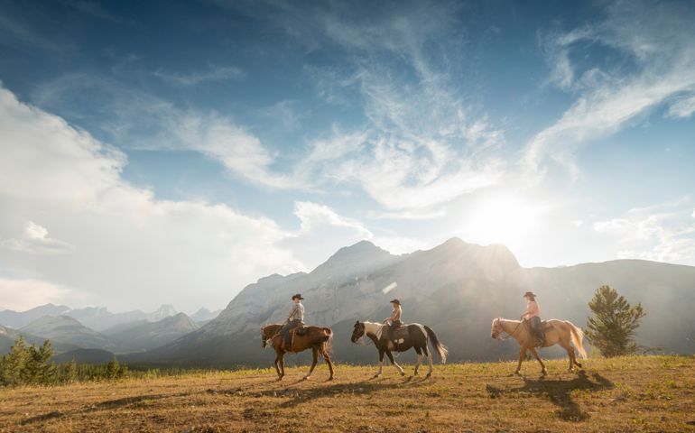 Three cowboys/cowgirls lead horses thru mountains