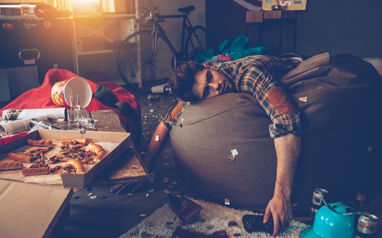Young handsome man passed out on bean bag with joystick in his hand in messy room after party