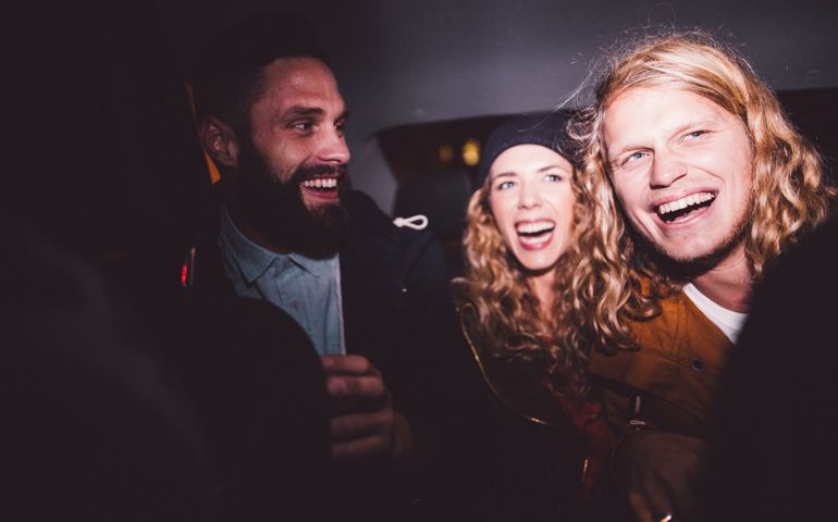 Three hipster young adult friends smiling and partying inside a car at night