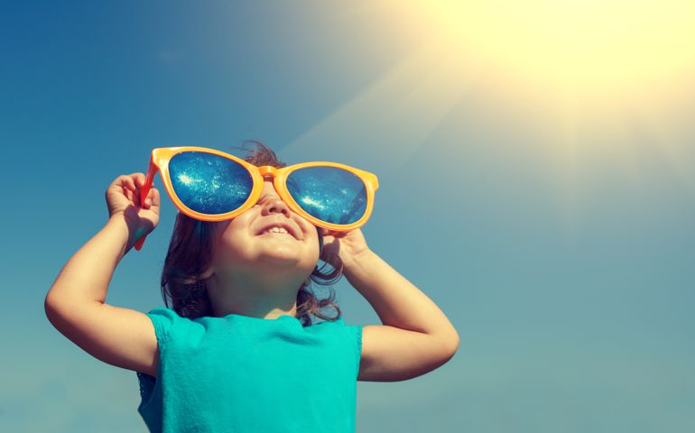 Happy little girl with big sunglasses looking at the sun
