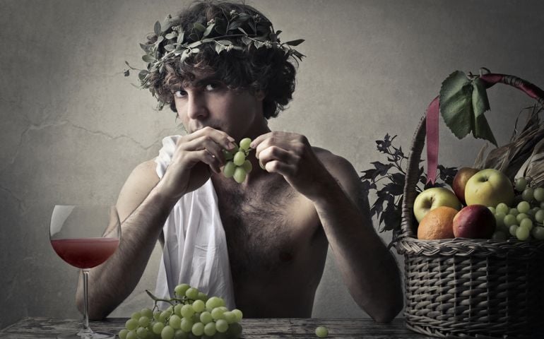 Man dressed like Dionysus eats a piece of grapes