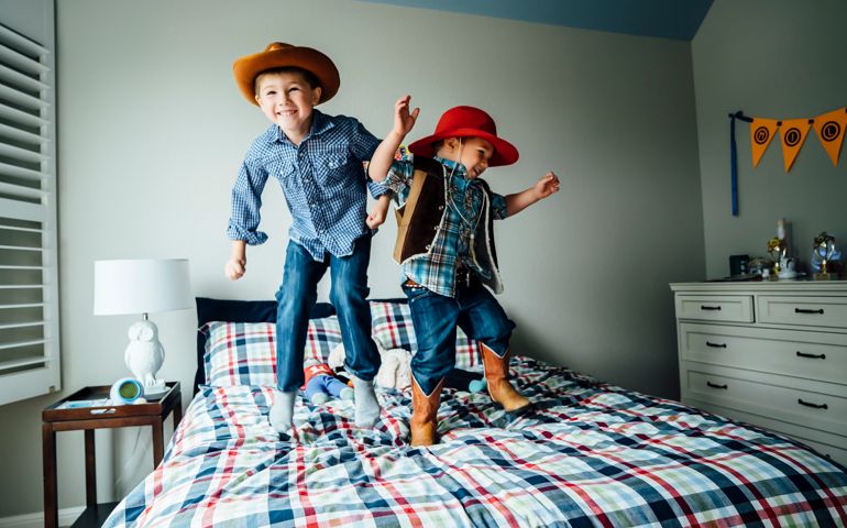 Caucasian boys wearing cowboy costumes jumping on bed