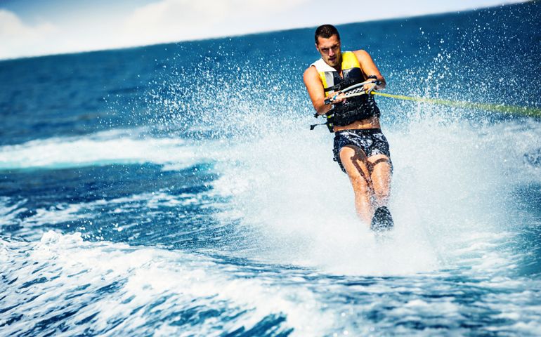 Closeup front view of a young man wakeboarding on a sunny summer day at open sea. He's wearing swimming suit and a life jacket.