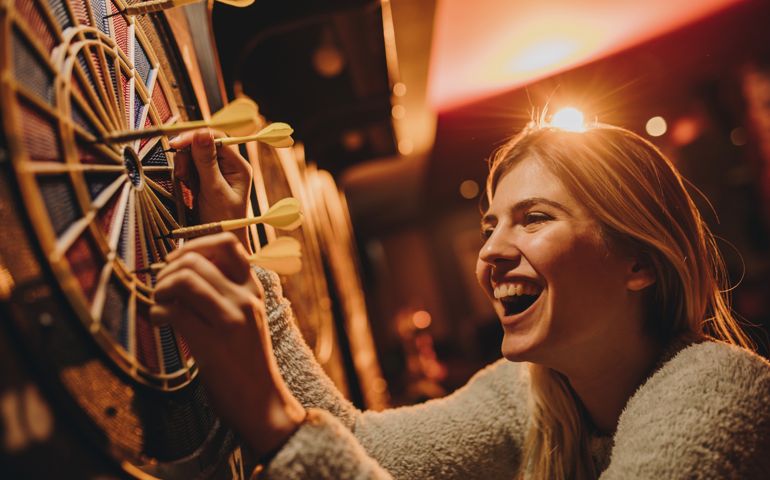 Young happy woman removing darts out of dart board in entertainment club.