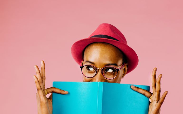 Portrait of a young woman holding a blue note book and looking up, full of joy and happiness, isolated on pink studio background