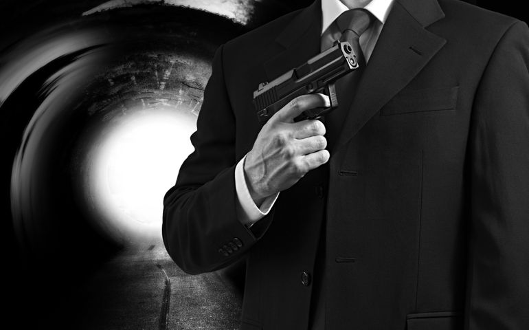 A secret agent holding a gun against a tunnel background with a bright light.