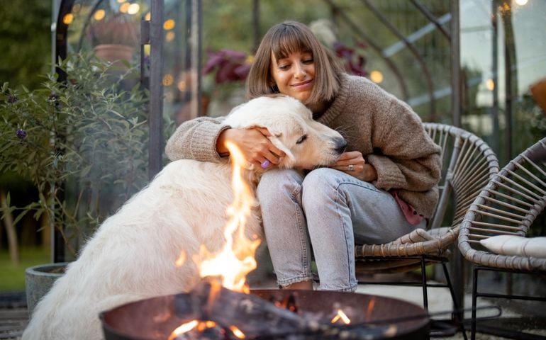 Young woman spends evening time with her cute white dog, sitting by the fire in garden at cozy and beautiful atmosphere
