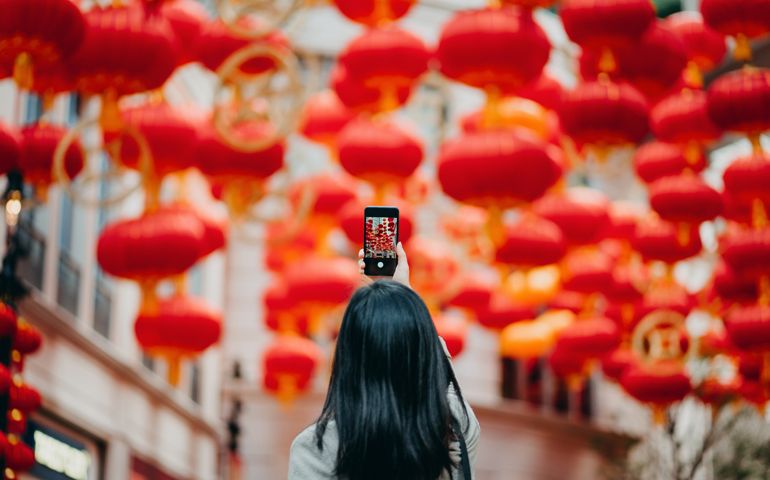 Rear view of woman taking photos of traditional Chinese red lanterns with smartphone on city street