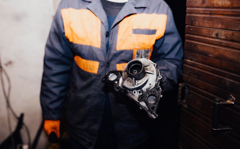 male master auto mechanic holds a car water pump in his hand.