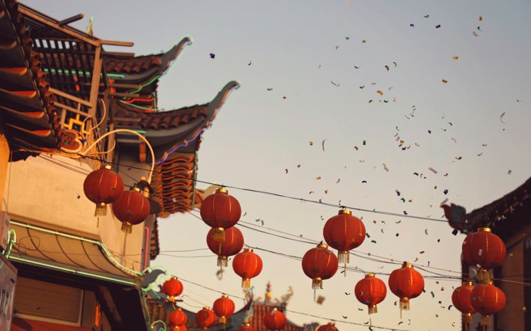 Looking up at rows of red Chinese lanterns and pagoda style architecture with the air filled with confetti in late afternoon warm sun on Chinese New Year.