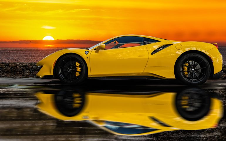 PHOTOGRAPH OF A YELLOW FERRARI AND ITS REFLECTION IN THE WATER WITH A BACKGROUND SUNSET