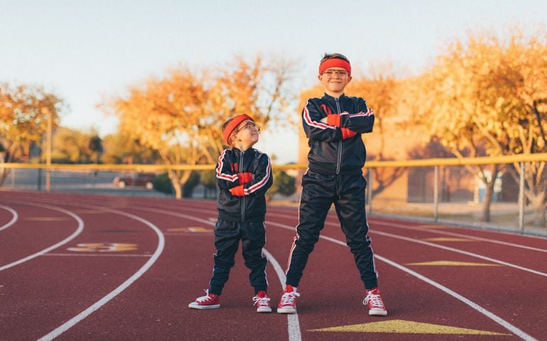 A young team of nerd boys are dressed in retro track suits and headbands stand on the running track ready to live a healthy lifestyle. The younger boy looks up to his older brother and positive example and role model. Image taken in Tempe, Arizona.