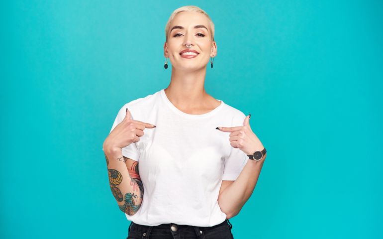 Studio shot of a confident young woman pointing at her t shirt against a turquoise background