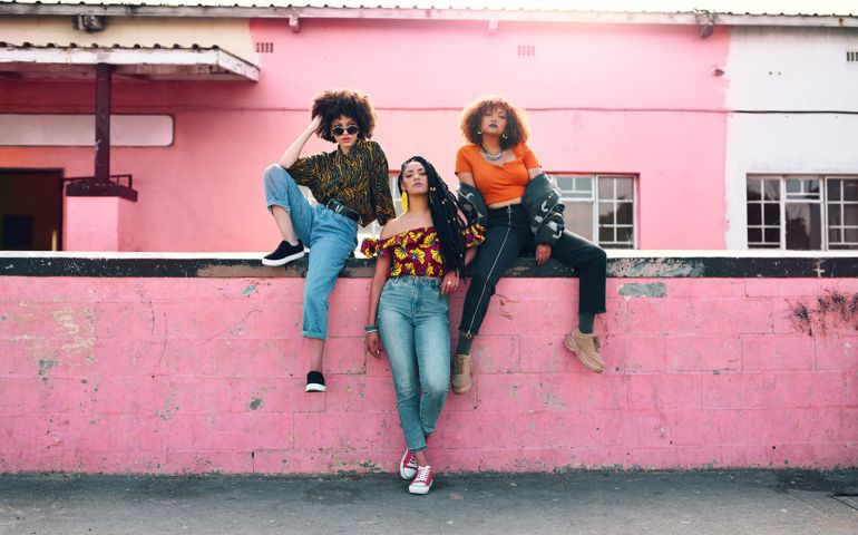 Full length shot of three attractive and stylish young women posing together against an urban background