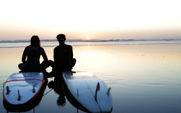 Young couple sat on surfboards at sunset