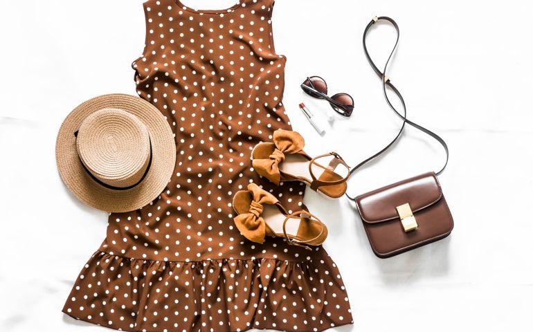 Summer brown polka dot sleeveless dress, suede sandals, leather crossbody bag, sunglasses and hat on a light background, top view
