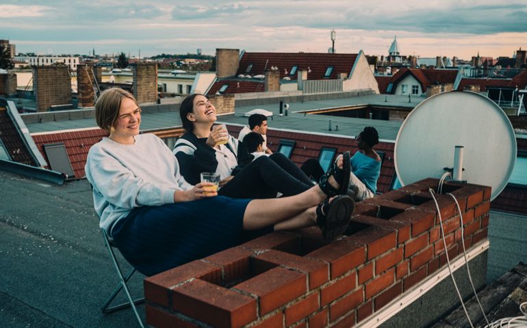 Smiling female talking to friend while enjoying drink on building terrace