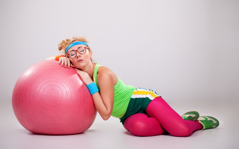 Tired nerdy fitness girl laying down on pink exercise ball