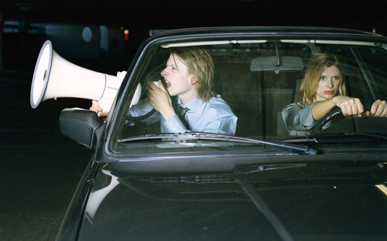Man and woman in car, man using megaphone through open window