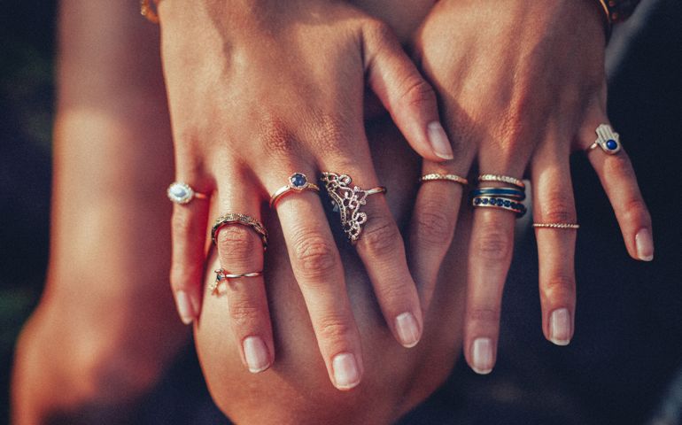Cropped closeup of a boho girl's hands with many rings on her fingers, in gold and silver with dark blue stones