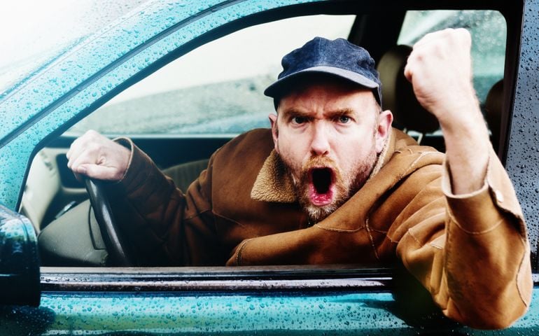 A furiously angry man driving a car yells and shakes his fist through the car window in a bout of uncontrollable road rage! He looks pretty scary!
