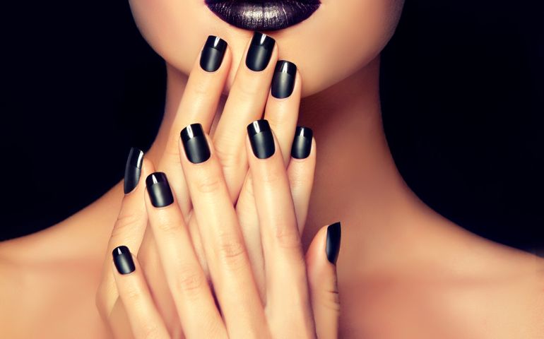 Beautiful woman-model is showing black french style manicure on the nails and black lipstick . Makeup and cosmetic.