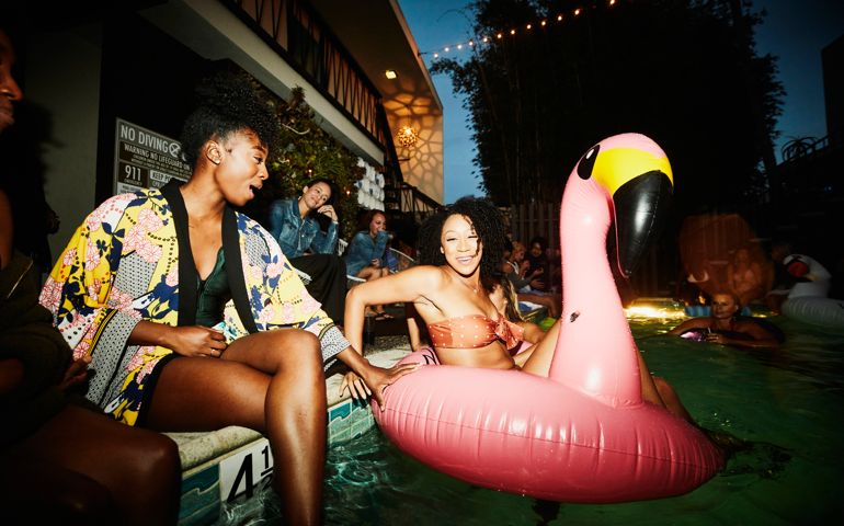 Smiling woman sitting in inflatable flamingo in pool during party with friends at hotel