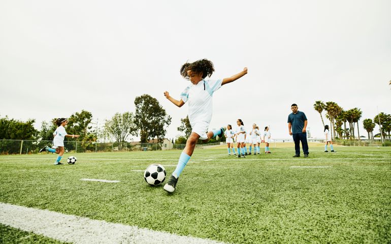 Coach watching young female soccer player practicing shot before game