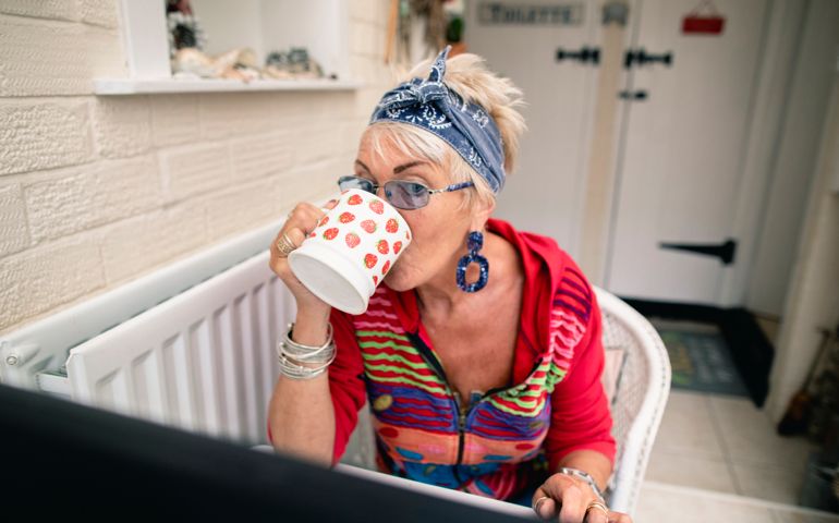 Senior woman sitting at her kitchen She is sitting laughing while enjoying a hot drink.