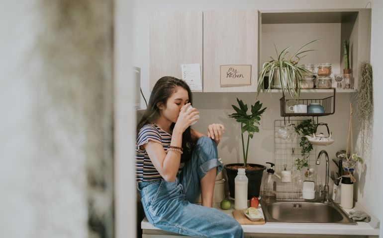 Thai hipster woman has a simple life of healthy living while drinking milk and sitting on the kitchen counter at home, Bangkok Thailand